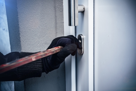 masked burglar with crowbar breaking and entering into a victim's home.