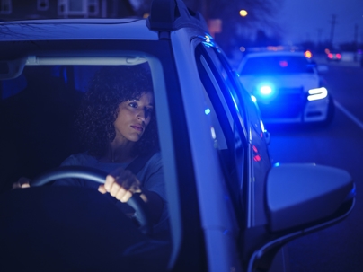 A young woman in a car, pulled over by a police officer at night.